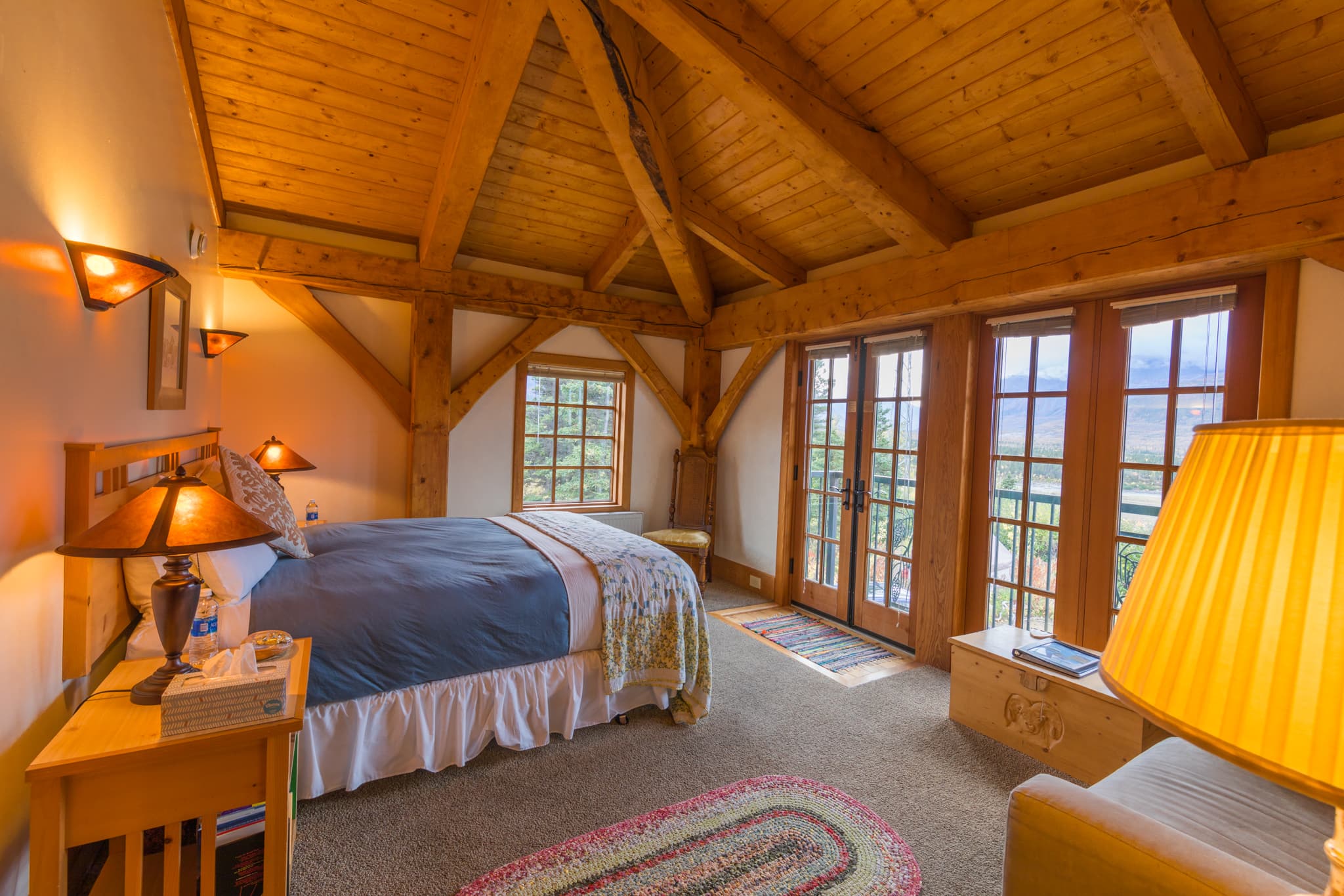 Cozy bedroom with wooden beams, a large bed, and large windows offering scenic views.