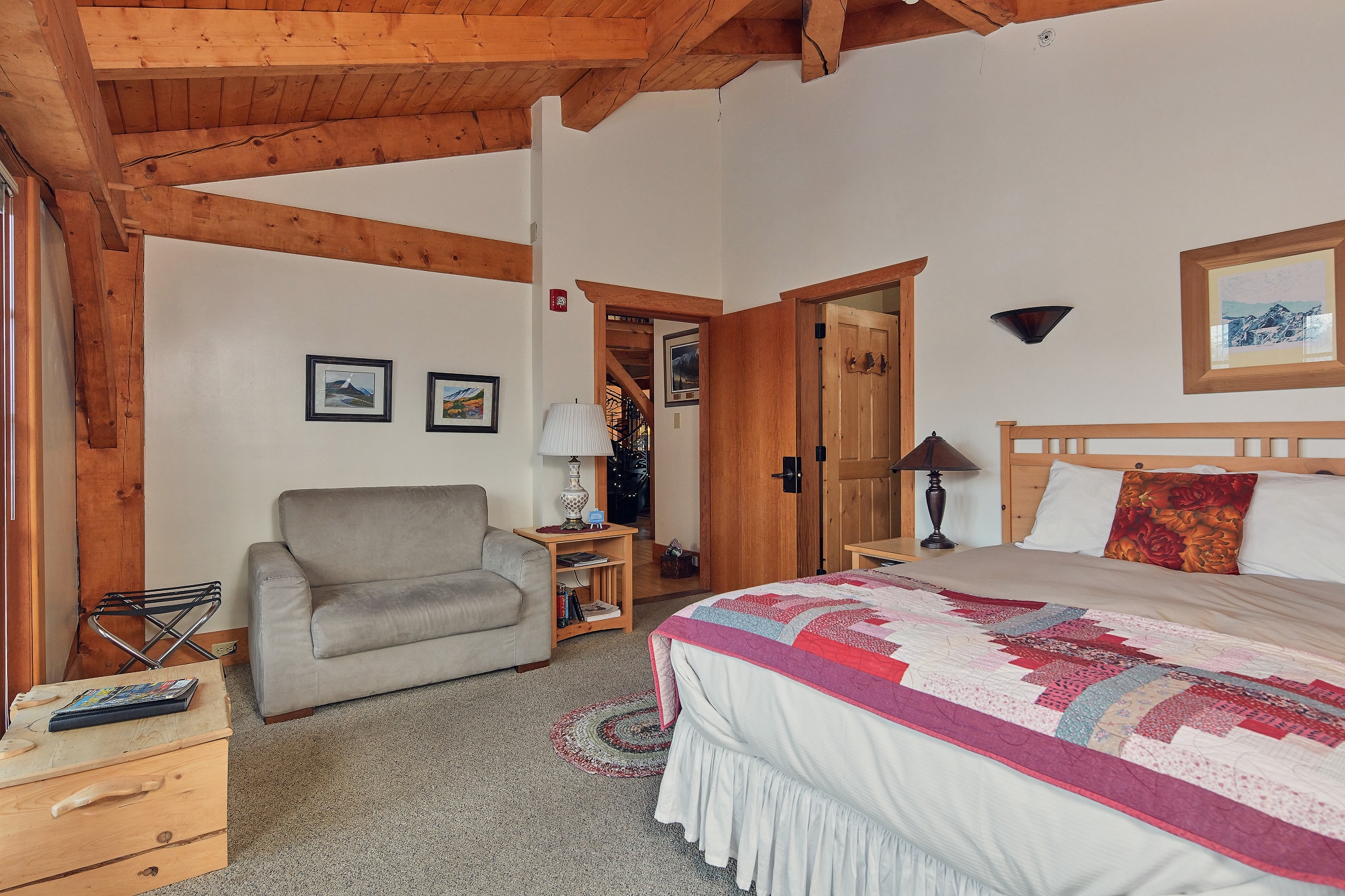 Cozy bedroom with wooden beams, a large bed, and a chair beside a warm ambiance.