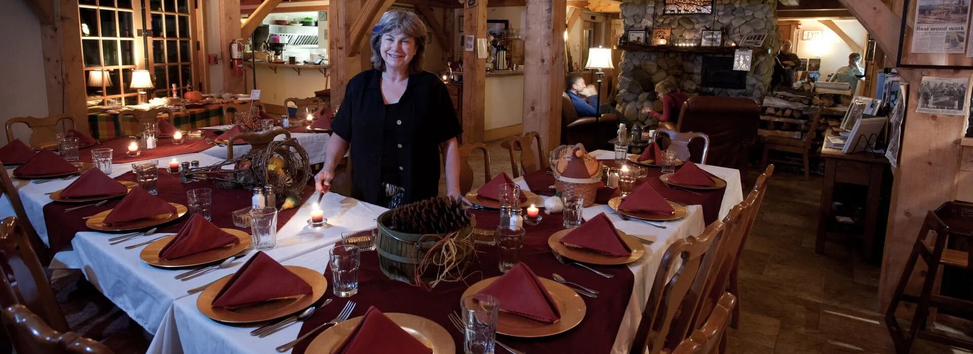 A woman stands beside a beautifully set dining table in a cozy, rustic restaurant.