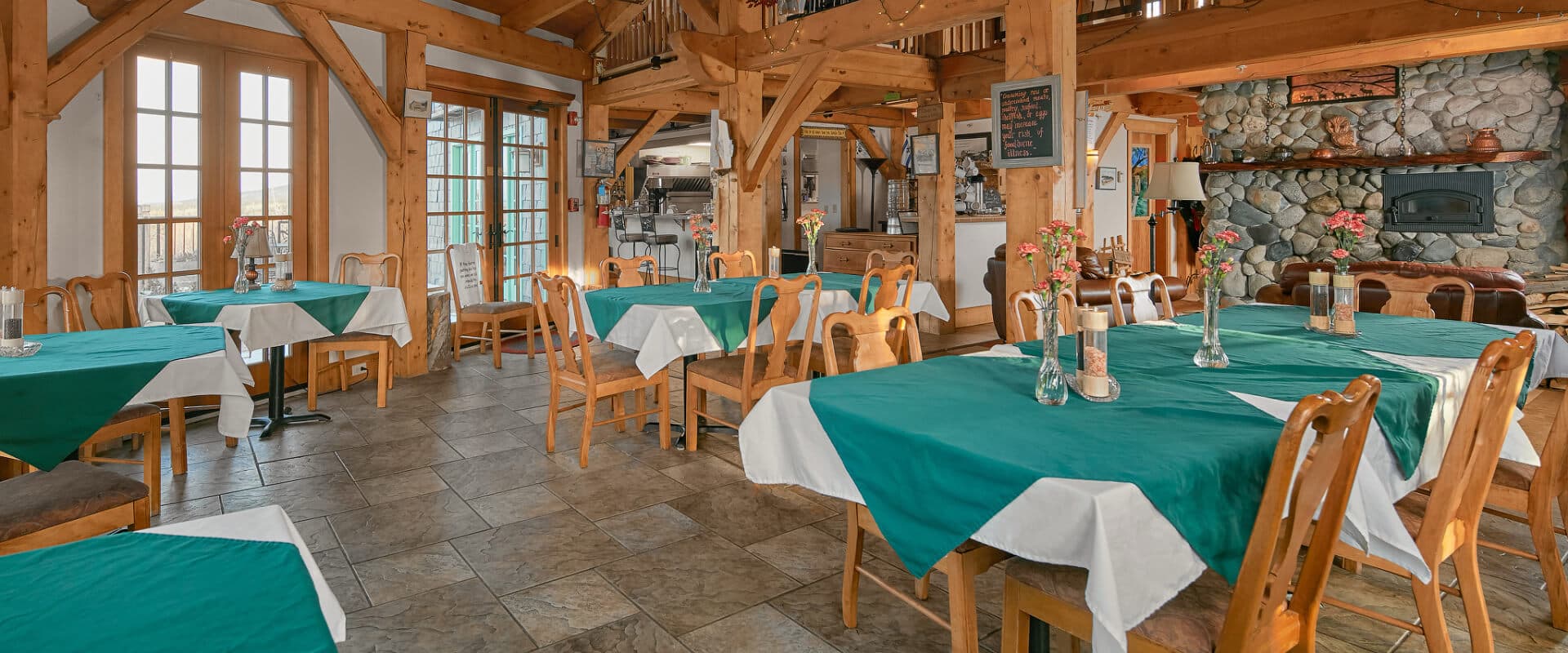 A cozy, wooden-beamed restaurant interior with tables set in teal and white linens.
