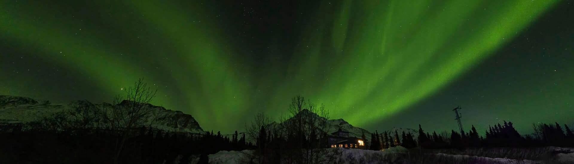 A vibrant display of the northern lights over a mountainous landscape and a cozy cabin.