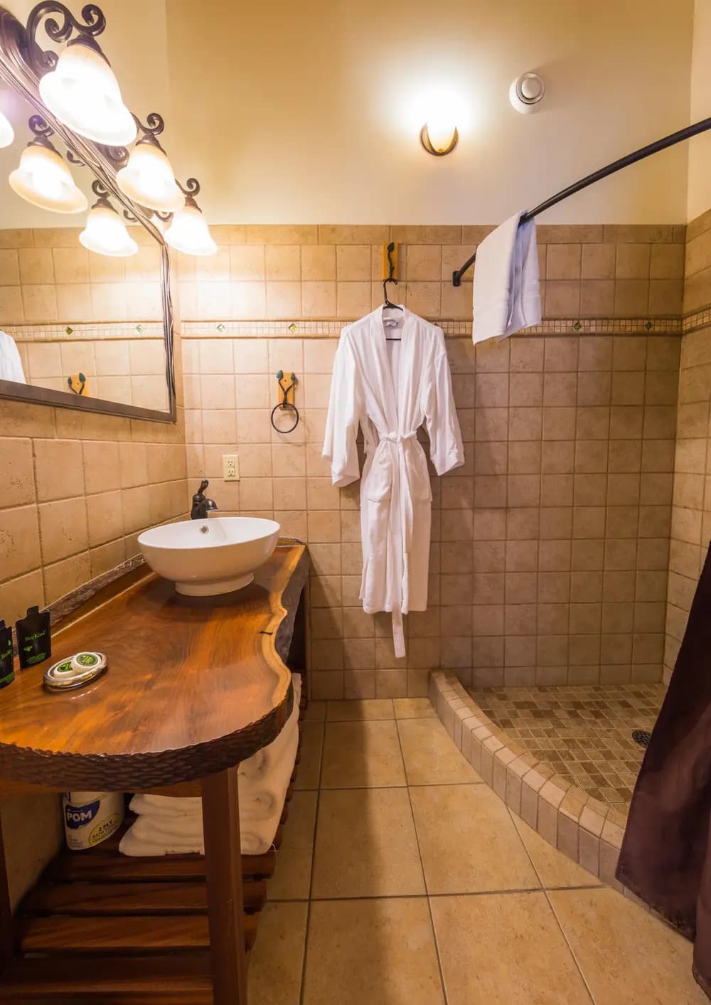 A cozy bathroom featuring a wooden countertop, a round sink, a shower, and a white robe hanging on the wall.