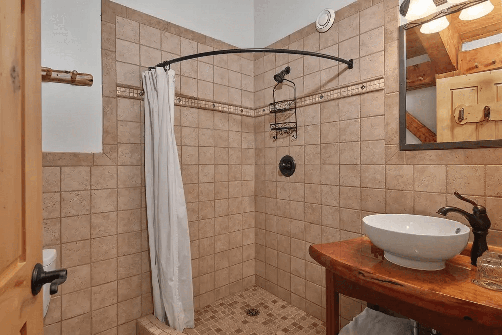 A modern bathroom featuring a tiled shower with a white curtain, a wooden sink vanity, and natural wood accents.