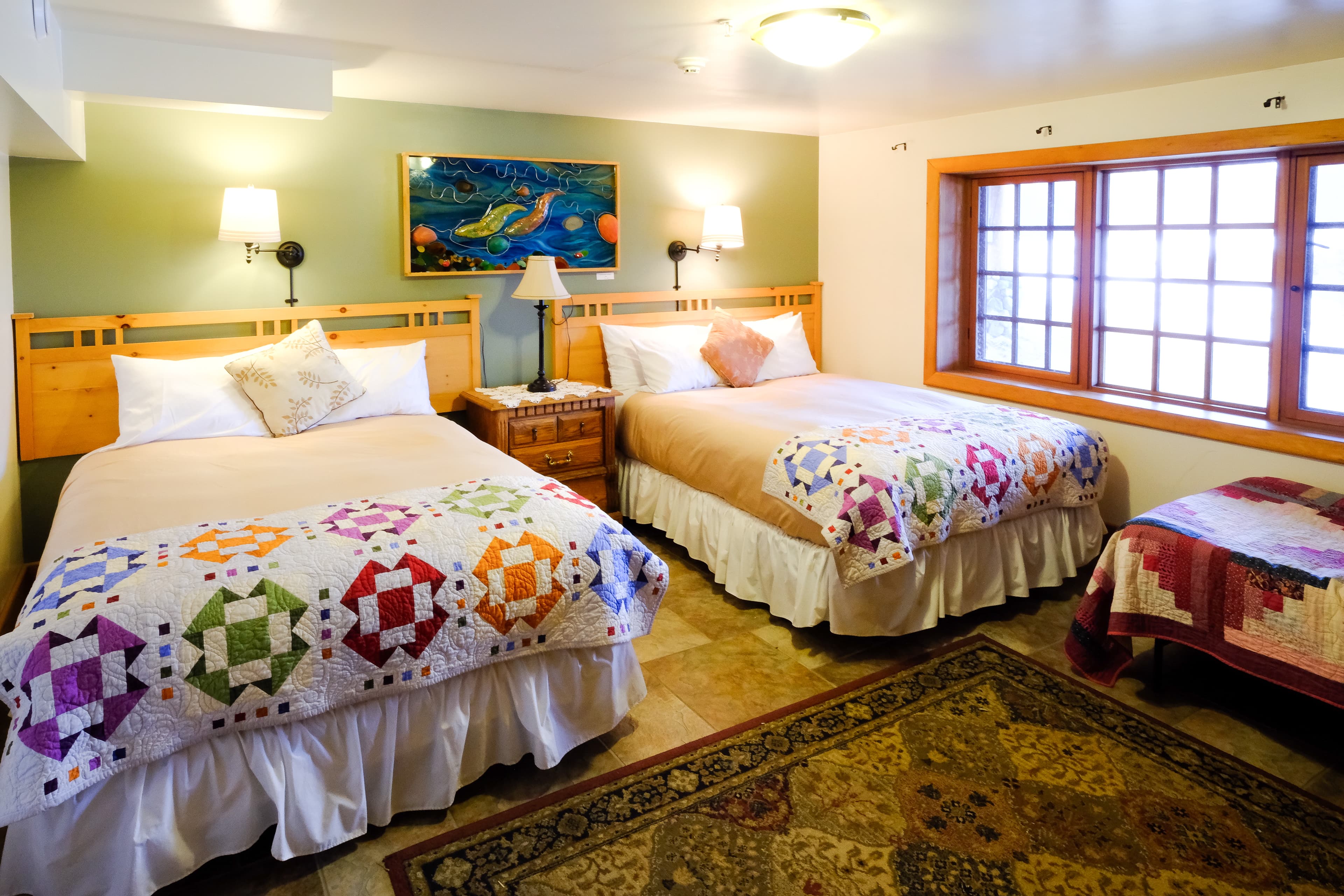 Cozy bedroom featuring two beds with colorful quilts and a large window.