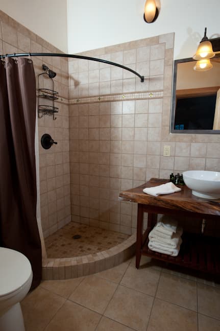 A modern bathroom with a tiled shower, wooden countertop, and neatly stacked towels.