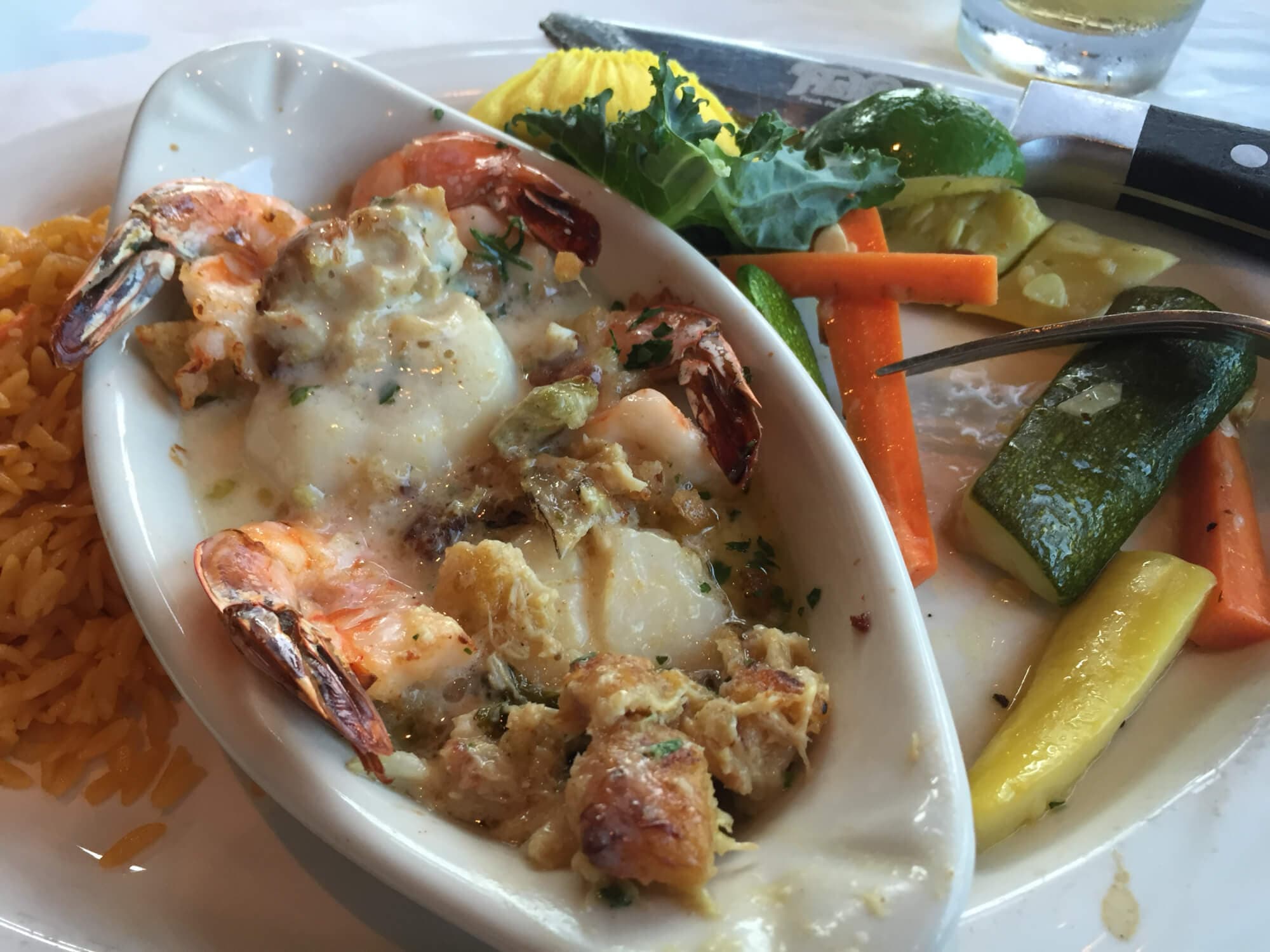 A seafood dish with shrimp, scallops, and vegetables served alongside rice.