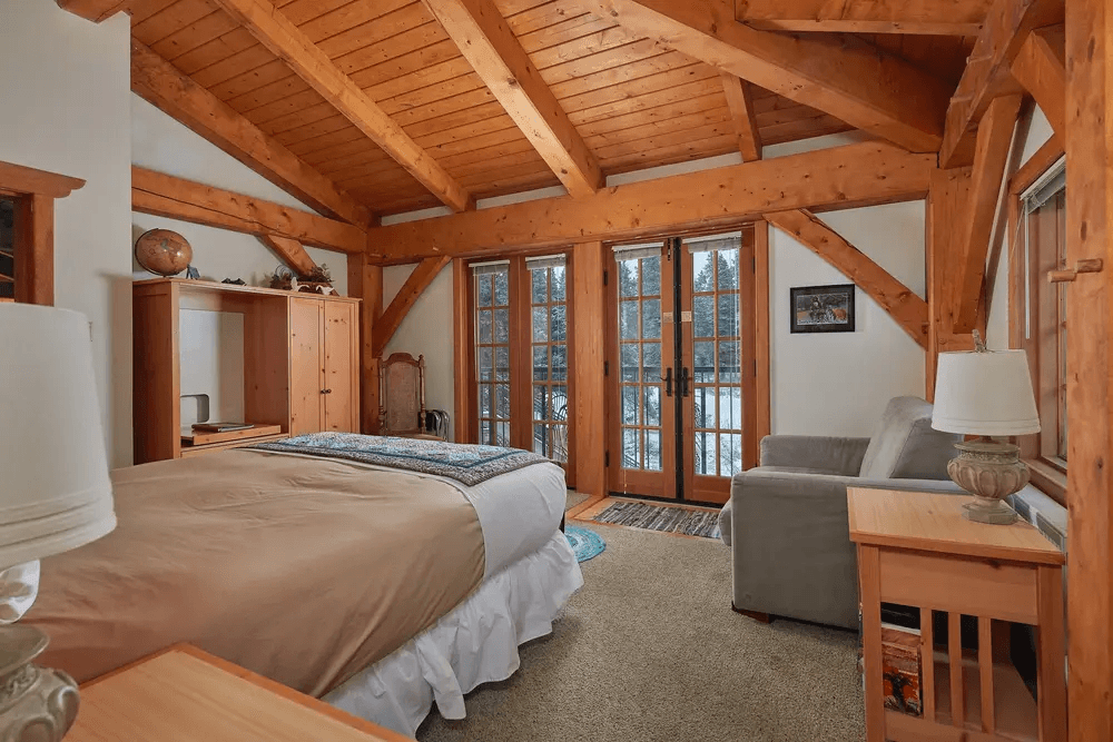 Cozy bedroom with wooden beams, a queen bed, and French doors opening to a snowy view.