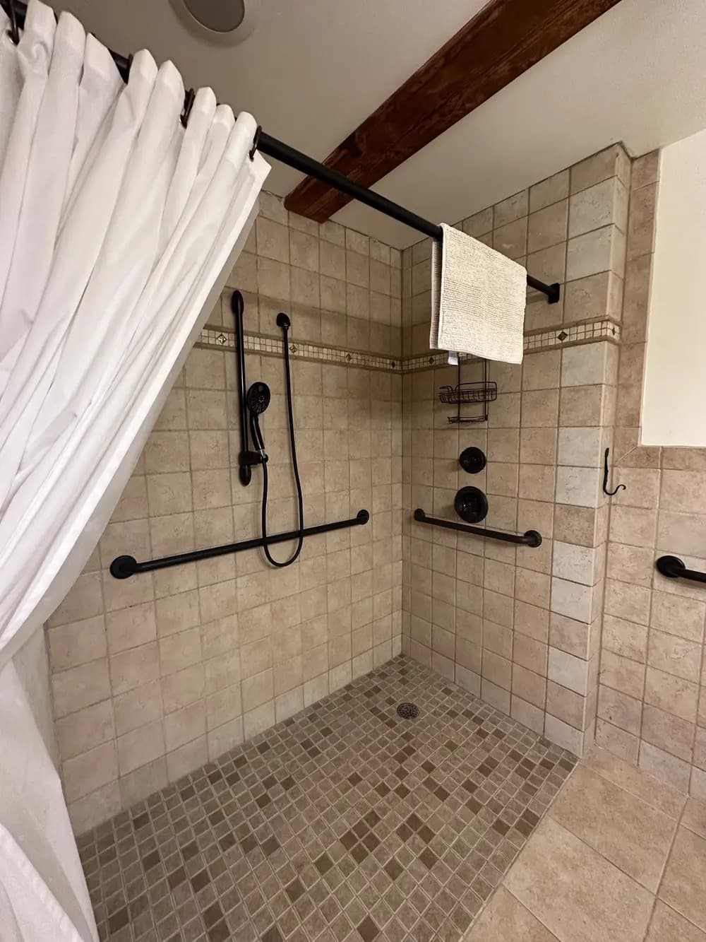 A tiled shower stall featuring grab bars, a handheld showerhead, and a shower curtain.