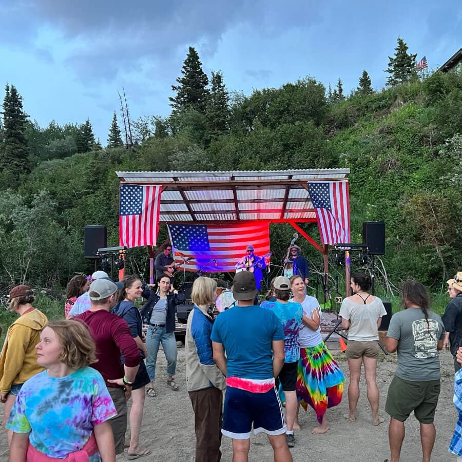 A lively outdoor concert features a band on stage adorned with American flags, while an audience enjoys the music.