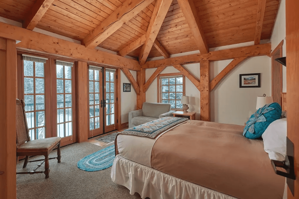 Cozy bedroom with wooden beams, a large bed, and French doors leading to a snowy view.