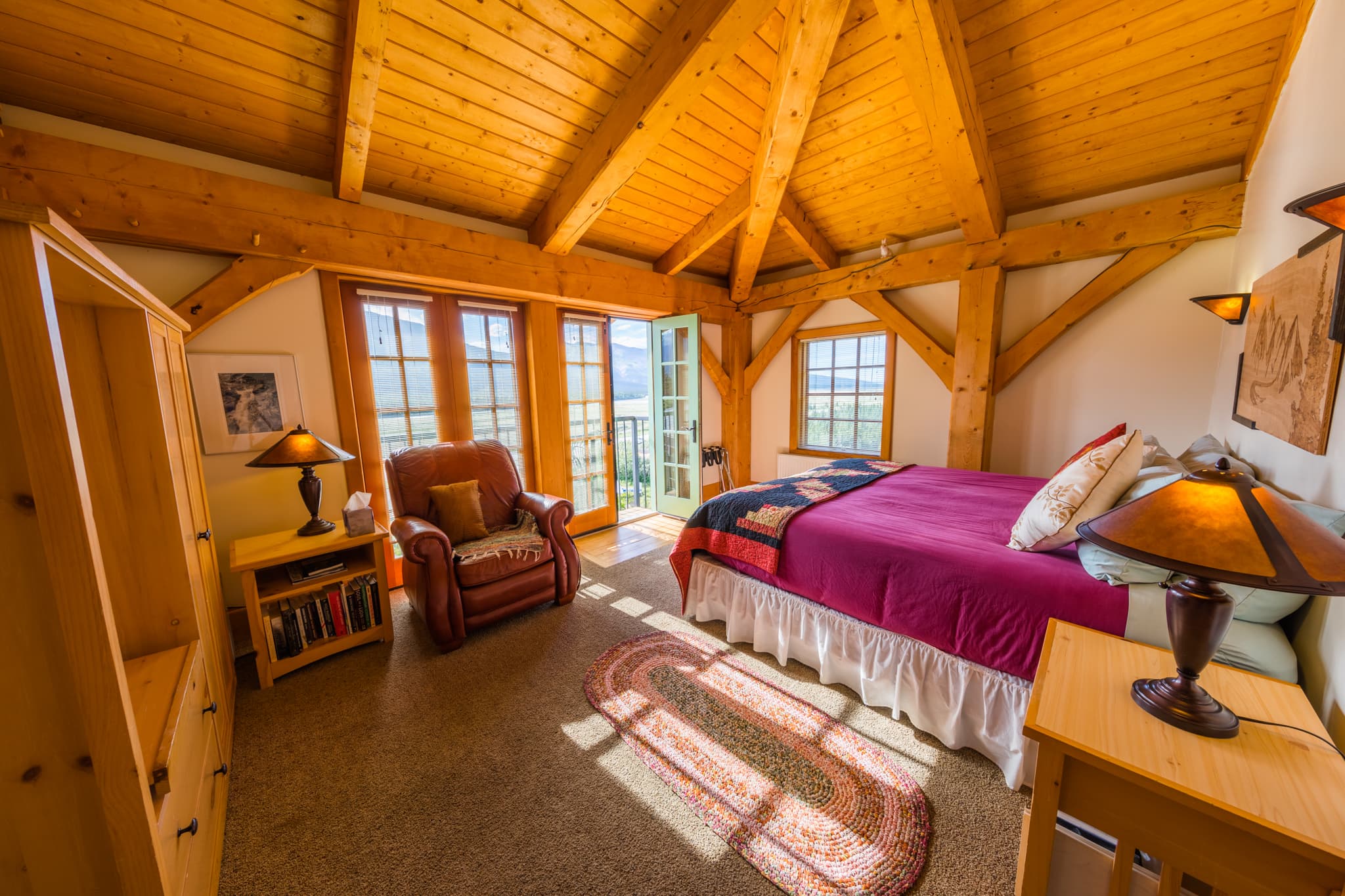 Cozy bedroom with wooden beams, a large bed, and a scenic view through open doors.