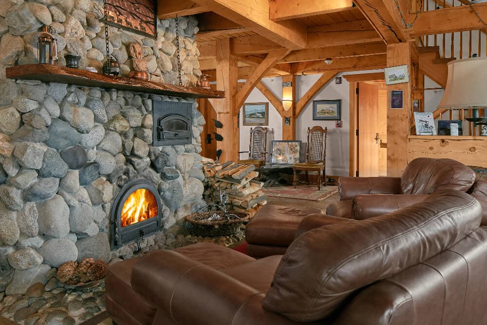 A cozy living room featuring a stone fireplace, leather sofas, and wooden beams.