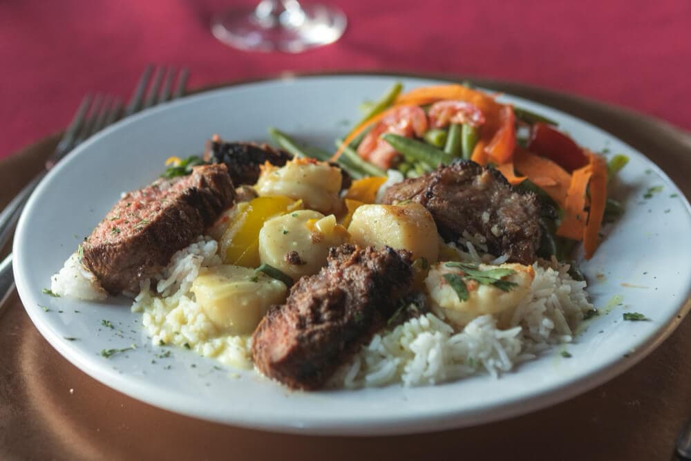 A plate of rice topped with grilled meat, assorted vegetables, and garnished with herbs.